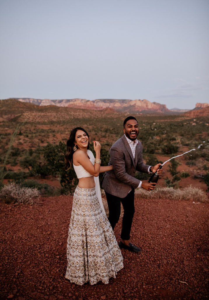 bride-and-groom-popping-open-a-bottle-of-champagne-and-laughing-in-Sedona-Arizona