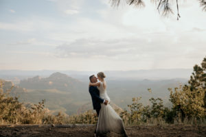 Bride and groom at the Sedona elopement on the edge of a cliff during sunset.
