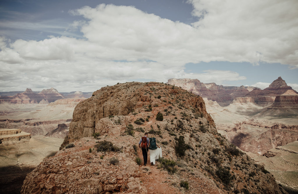 bride and groom hiking in wedding clothes at their elopement in the grand canyon