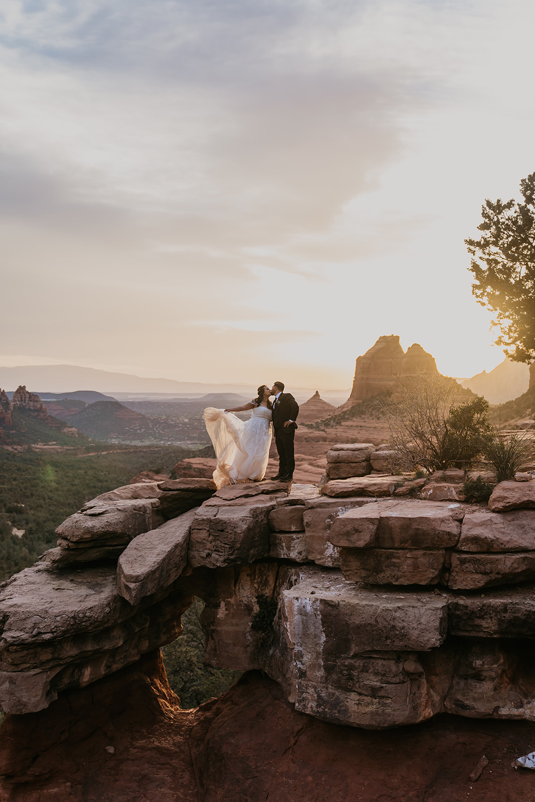 bride and groom kissing on a cliff edge with the sunset in the background at merry go round rock in sedona arizona