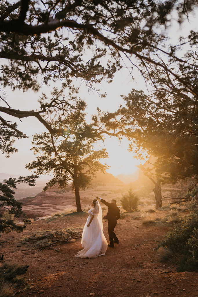 bride and groom dancing with a golden sunset in the background at their elopement at merry go round rock in sedona, arizona