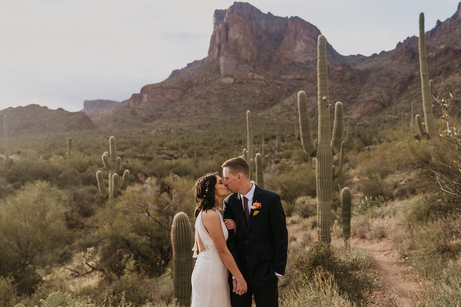 bride and groom hugging next to saguaro cactus with mountains in the background at their elopement in phoenix, arizona