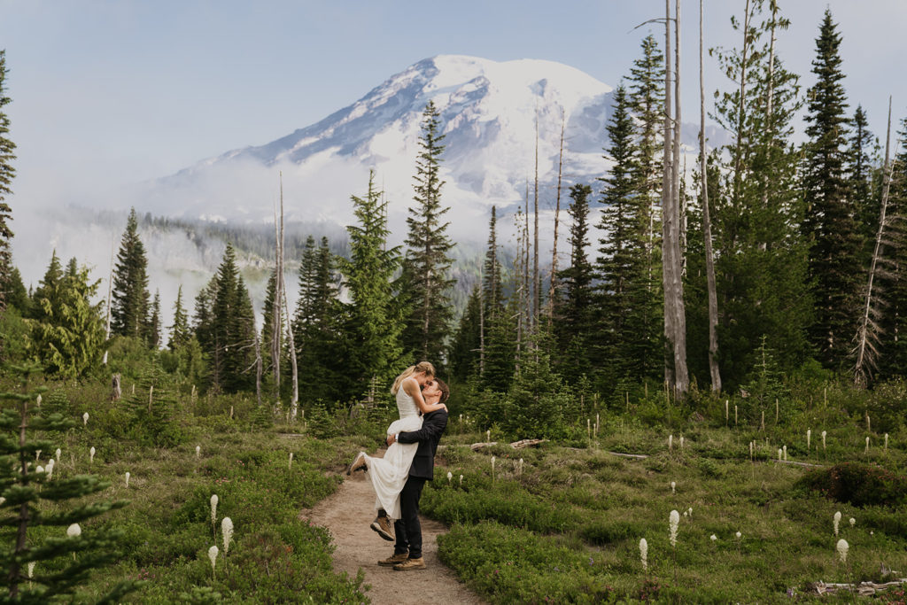 bride is being picked up and spun around with the view of mount rainier in the background on their wedding day

