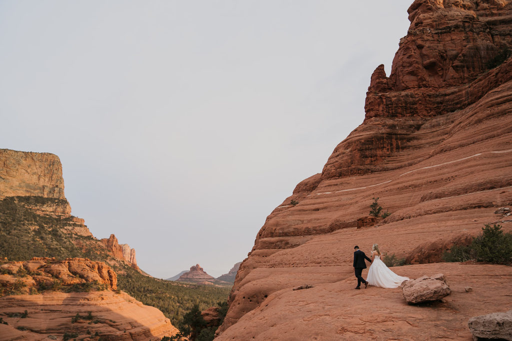 bride and groom hiking on cliff edge at their elopement in sedona arizona