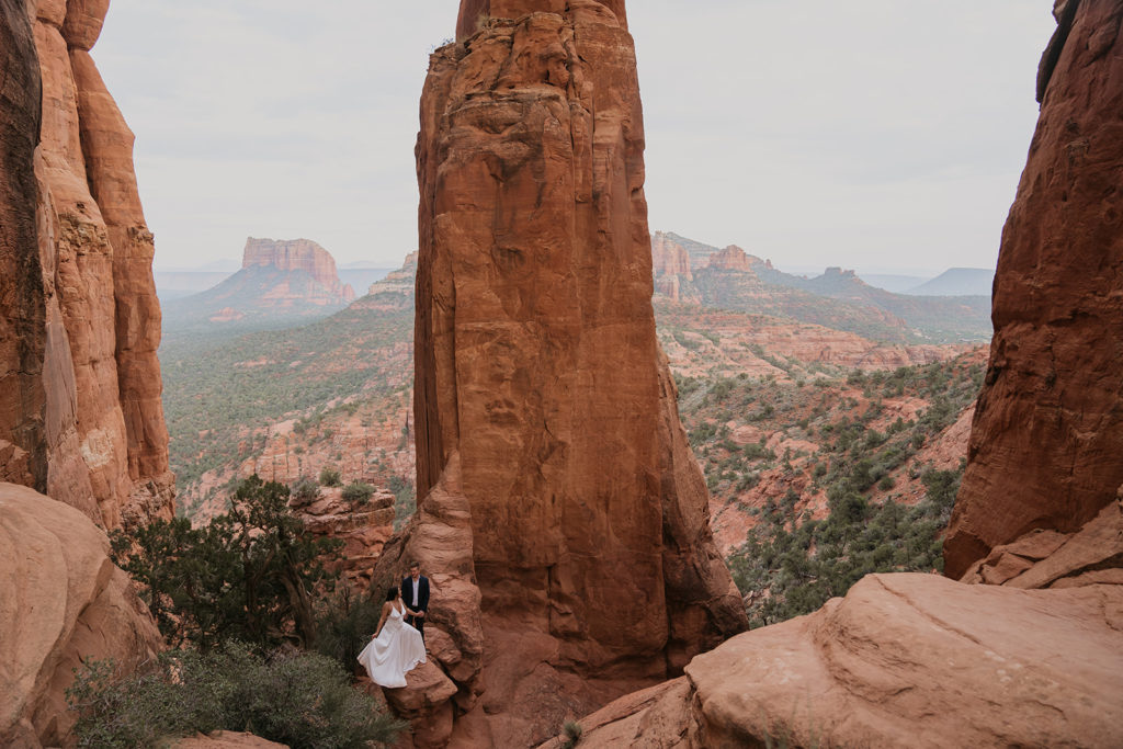 bride and groom sitting on cliff edge at their elopement in sedona arizona