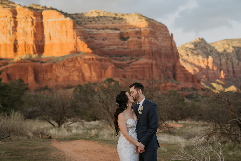 bride and groom kissing at sunset with the red rock mountains of sedona in the background
