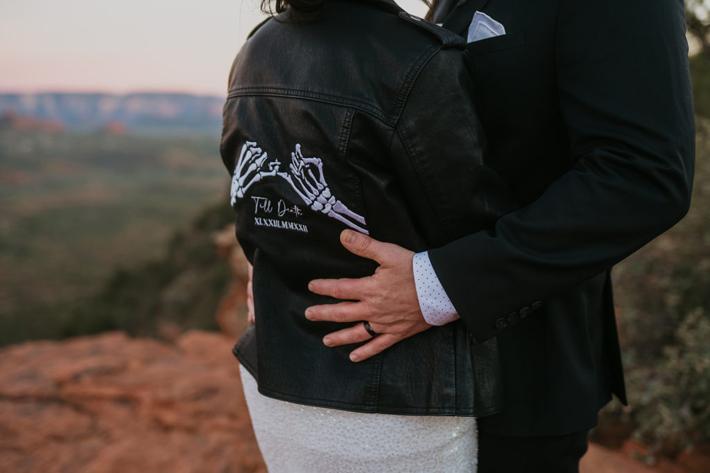 groom holding the waist of a bride with a bridal leather jacket on
