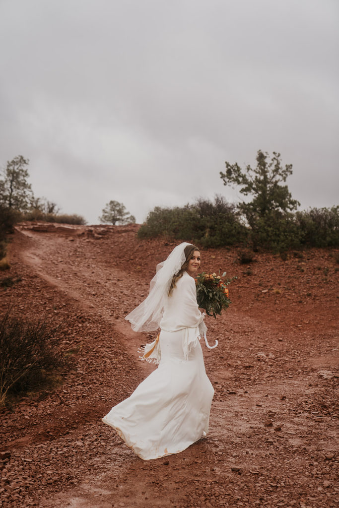 bride looking and smiling at the camera while walking in her wedding dress and veil in the rain