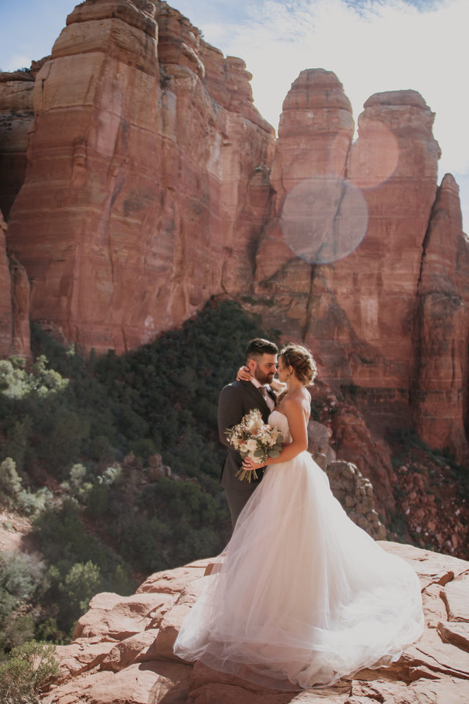 bride and groom holding each other close on cliff in sedona arizona